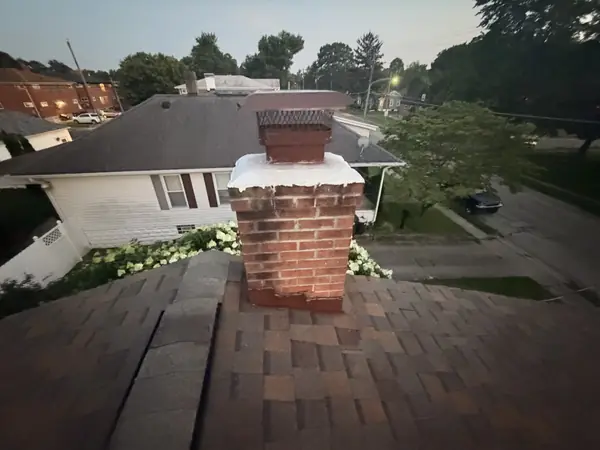Brick chimney with a sealed crown on an asphalt shingle roof at dusk