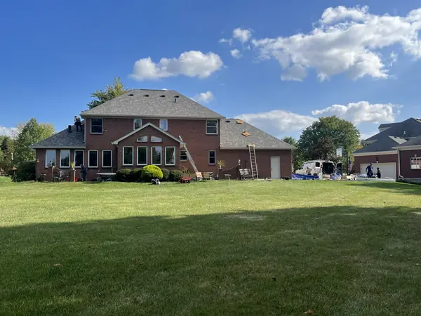Roof replacement underway on a large brick colonial with ladders on the rear elevation