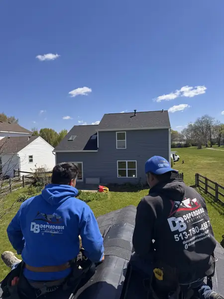Two roofers installing ridge cap shingles on a suburban home