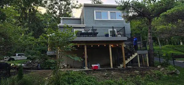 New elevated deck with stairs and black railing on the back of a hillside home