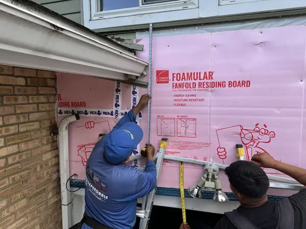 Installers fastening fanfold residing board insulation before new siding