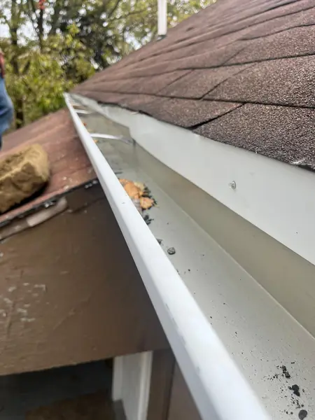 White gutter being cleared of debris under asphalt shingles