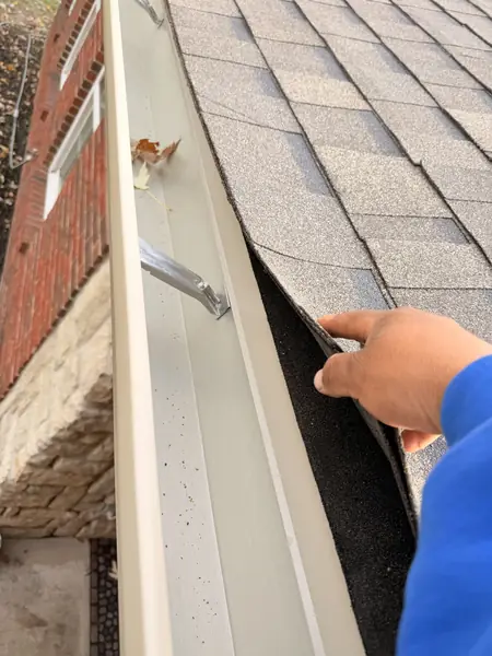 Inspecting the gutter and drip edge where shingles meet the brick wall