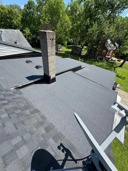 Newly installed low-slope roof tying into architectural shingles around a block chimney