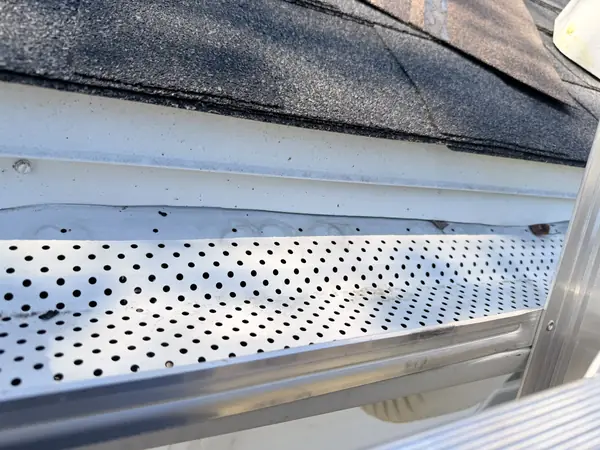 Close-up of a perforated aluminum gutter guard under the shingle edge