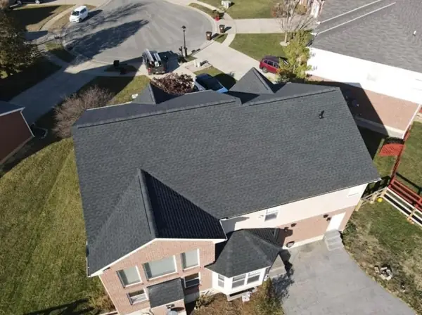 Drone view of a finished black architectural shingle roof on a two-story brick home in a cul-de-sac