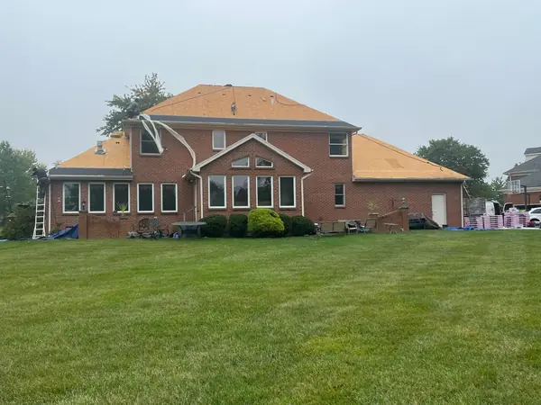 Rear of a large brick home with new roof decking installed before underlayment and shingles
