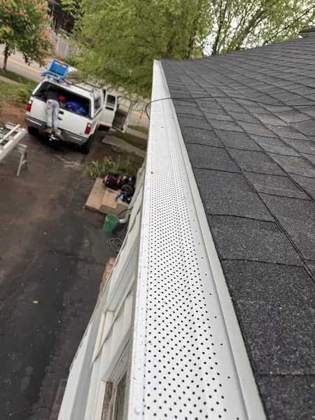 Perforated gutter guards installed along a dark shingle roof edge