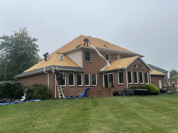 Crew installing new roof decking on a two-story brick home before shingles