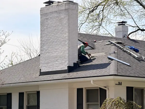 Crew replacing shingles around a tall painted brick chimney