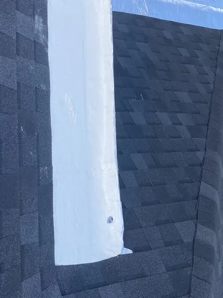 Roof valley sealed with a white elastomeric coating between dark shingles