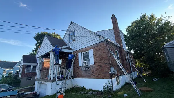 Crew on ladders installing white siding on the gables of a brick cape cod home