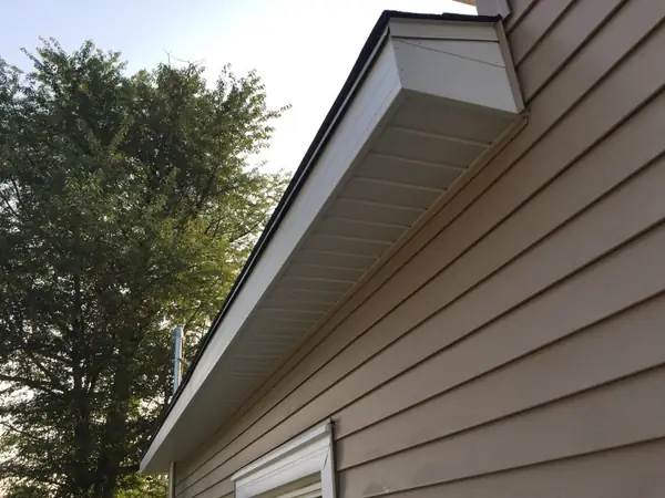 Clean soffit and fascia wrap on a gable eave above tan siding