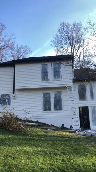 Two-story home getting new white siding with windows masked for protection